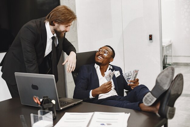 African man in a black suit. Guy sitting at the table. Businessman with money. International partners.