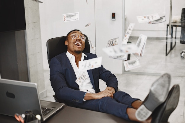 Free photo african man in a black suit. guy sitting at the table. businessman with money.