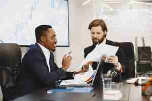 Free photo african man in a black suit. international partners. people sitting at the table with laptop.