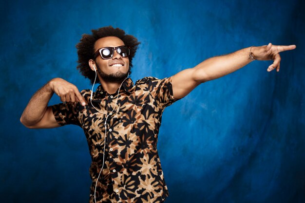 アフリカの男性がヘッドフォンで音楽を聴く、青い壁を越えて踊る。