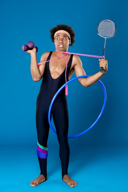 Free photo african man posing with dumbbells, hoop, skipping rope, racket