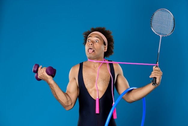 African man posing with dumbbells, hoop, skipping rope, racket