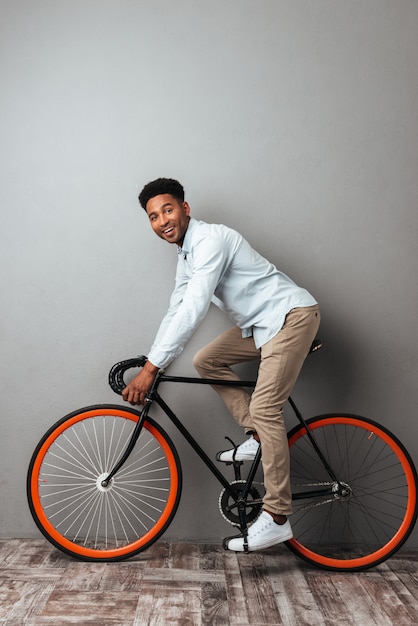 Uomo africano che controlla parete grigia con la bicicletta.