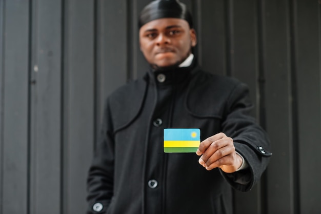 Африканский мужчина носит черный дураг, держит флаг Руанды под рукой, изолированный темный фон