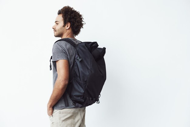 African man with backpack standing back to camera looking in side.