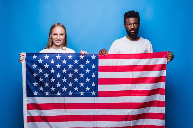African man with caucasian woman holding american flag isolated on blue wall