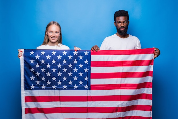 파란색 벽에 고립 된 미국 국기를 들고 백인 여자와 아프리카 남자