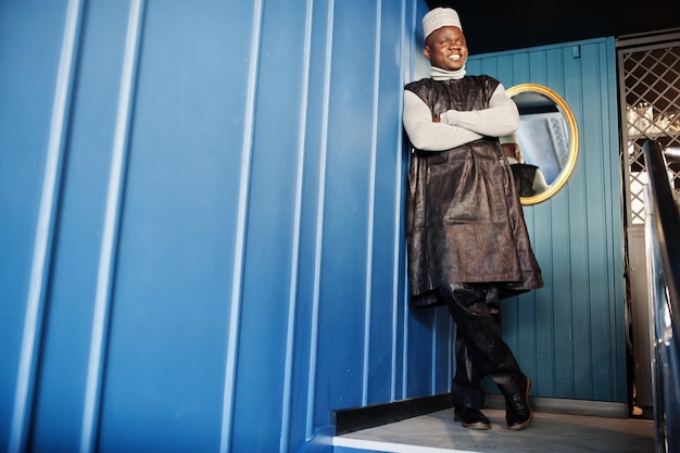 African men in black traditional clothes with cap against mirror on blue wall