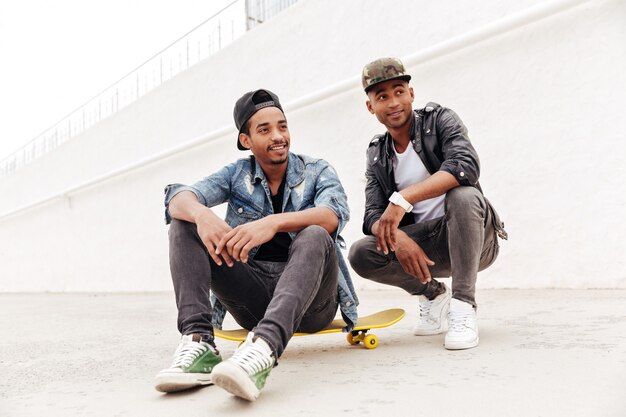 African men friends walking outdoors sitting with skateboard