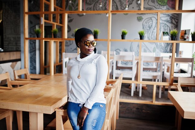 African muslim girl in black hijab and sunglasses posed at modern cafe