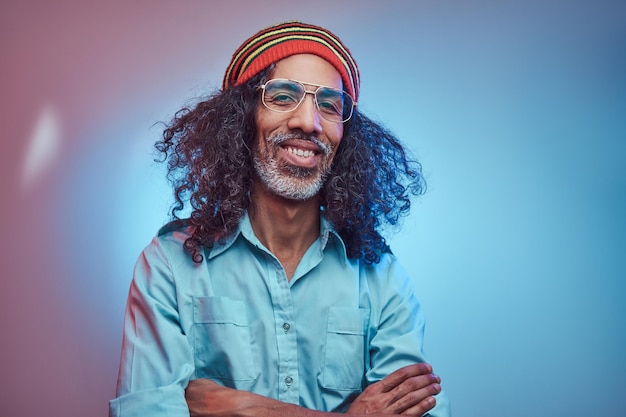 African Rastafarian male smiles and looks at the camera standing with his arms crossed. Studio portrait on a blue background.