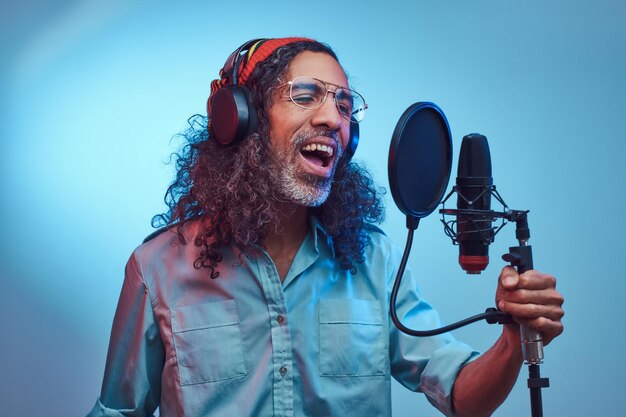 African Rastafarian singer male wearing a blue shirt and beanie emotionally writing song in the recording studio. Isolated on a blue background.