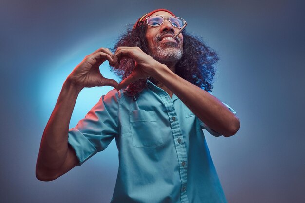 African Rastafarian smokes weed and showing heart symbol and shape with hands. Isolated on a blue background.