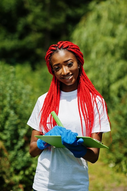 公園でクリップボードを持つアフリカの赤い髪のボランティアの女性は、慈善団体の人々とエコロジーの概念をボランティアします