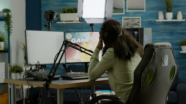 Free photo african streamer regrets losing live space shooter game tournament touching temple, chatting with team. professional gamer streaming online video games with new graphics on powerful computer.