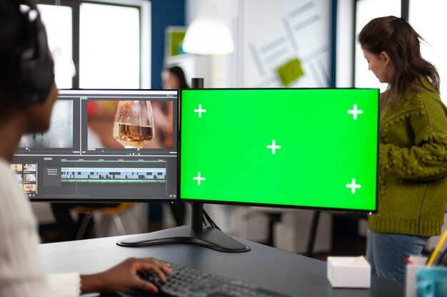 녹색 화면이 있는 PC를 사용하여 푸티지를 편집하는 헤드셋이 있는 아프리카 비디오 편집기