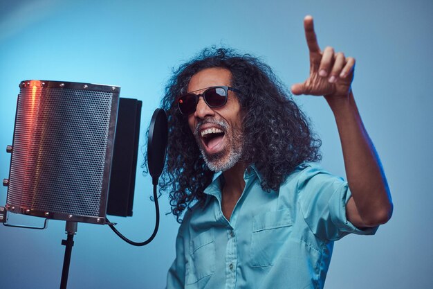 African vocal artist wearing a blue shirt emotionally writing song in the recording studio. Isolated on a blue background.