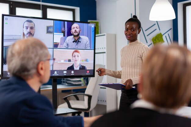 African woman discussing with remote managers on video call presenting new partners on webcam. Business people talking to webcam, do online conference participate internet brainstorming, distance office