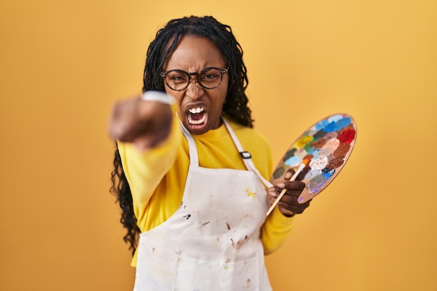 Free photo african woman holding painter palette pointing displeased and frustrated to the camera angry and furious with you