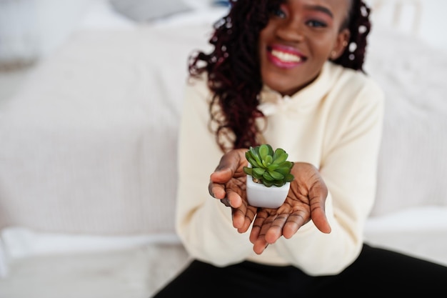 パーカーのアフリカの女性は家で小さな植木鉢を保持します