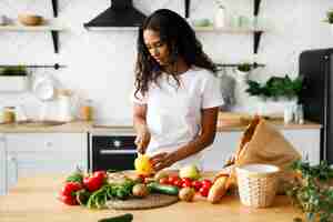 Free photo african woman is cutting a yellow pepper on the kitchen desk and on the table are products from a supermarket