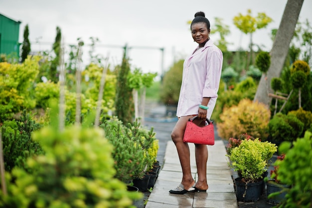 African woman in pink large shirt posed at garden with seedlings