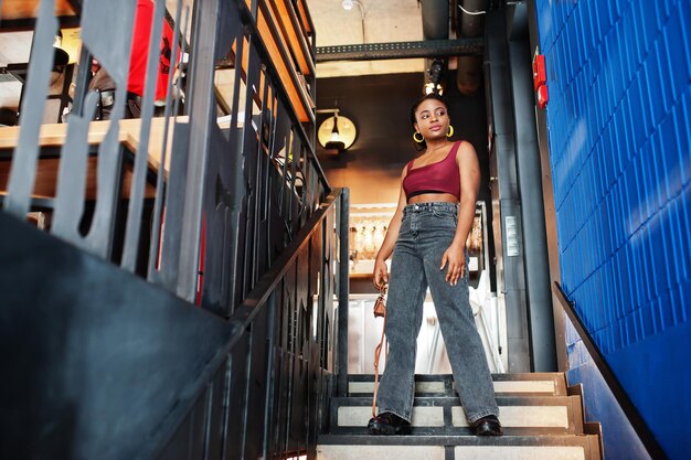 African woman in red marsala top and jeans posed indoor