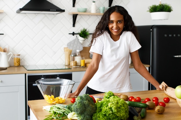 アフリカの女性は、さまざまな野菜や果物のキッチンデスクの前に立っています。