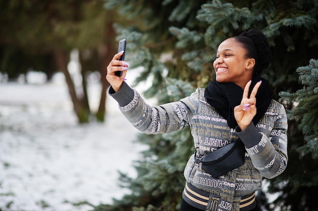 아프리카 여성은 유럽에서 겨울날 검은 스카프를 두르고 손에 휴대전화를 들고 셀카를 찍는다.