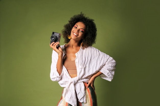 African woman with bright make up holding retro photo camera and laughing.