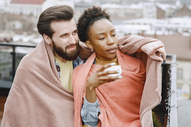 Foto gratuita donna africana con marito. ragazzo e ragazza in un plaid. amanti che bevono caffè sul balcone.