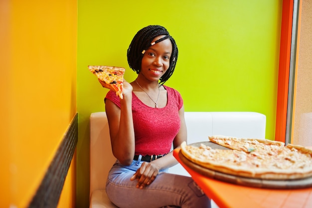 African woman with pizza sitting at bright colored restaurant