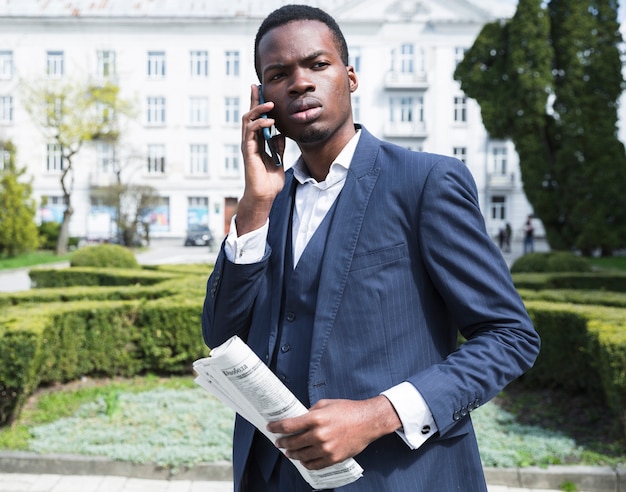 An african young businesswoman holding newspaper in hand talking on smartphone