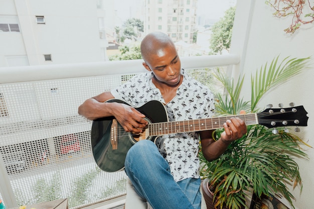 Giovane africano che gioca la chitarra che si siede nel balcone