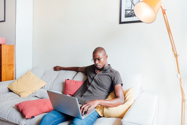 An african young man relaxing on sofa using laptop at home