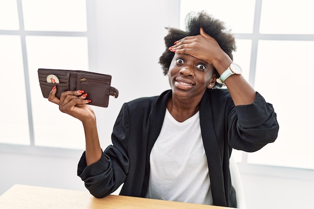 Бесплатное фото Африканская молодая женщина, держащая кошелек с виртуальной валютой биткойн, напряженная и расстроенная, положив руку на голову, удивленное и злое лицо