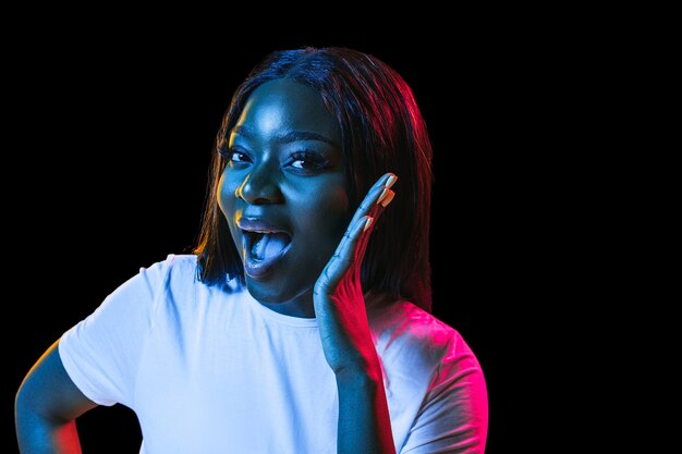 African young woman's portrait on dark studio background in neon Concept of human emotions facial expression youth sales ad