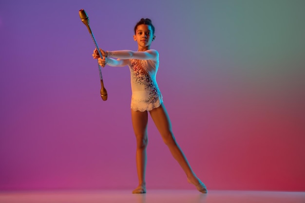 Africanamerican rhythmic gymnast pretty girl practicing on gradient studio background in neon light