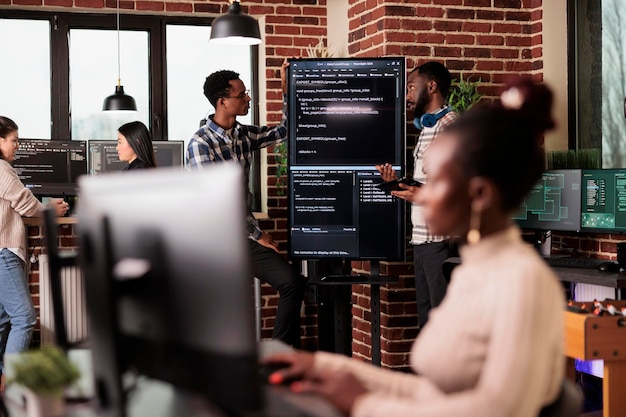 Free photo africann american system engineers analyzing source code looking for errors, checking big tv monitor in it agency office. software developers working on cyber security innovation in it agency.