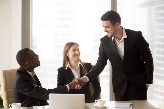Afro american and caucasian cheerful businessmen handshaking at