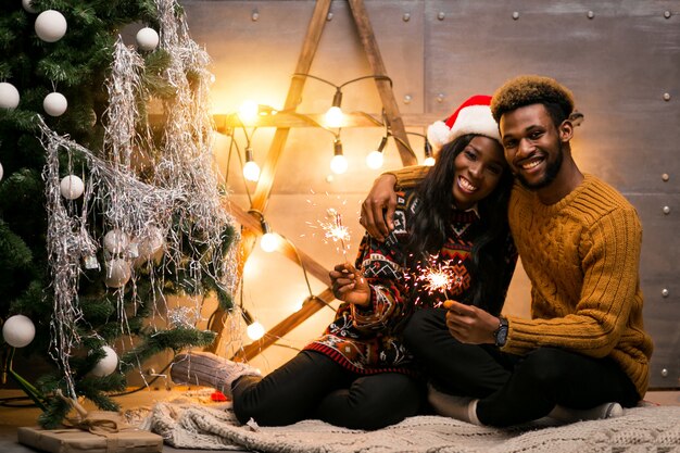 Afro american couple sitting with bengal lights by the Christmas tree