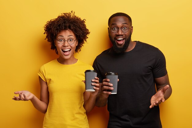 Afro American female and male friend meet together, have coffee from disposable cups