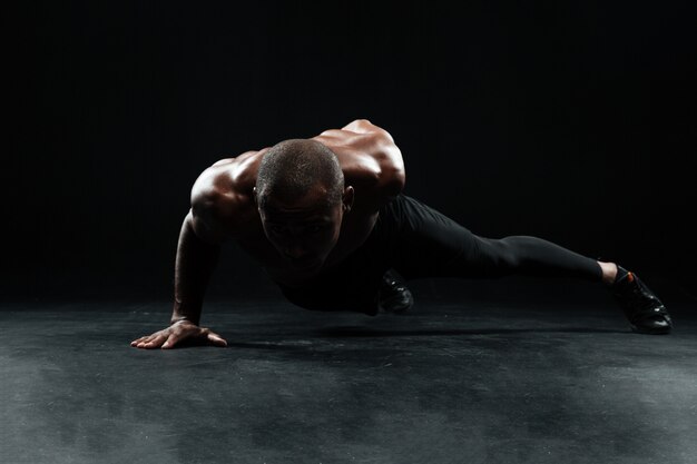 Afro american male athlete with beautiful muscular body doing one-handed push-ups exercise on floor
