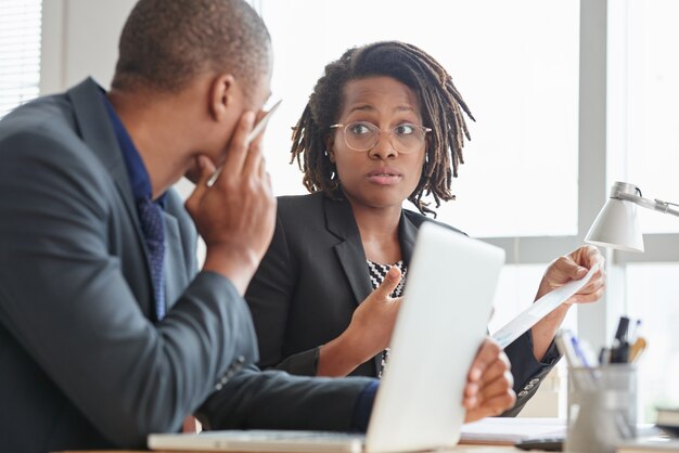 Afro-American male and female colleagues in suits talking in office