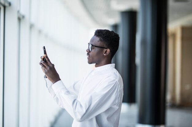 アフリカ系アメリカ人の男性がオフィスで写真を撮るスマートフォンで自分撮りを話している