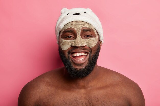 Afro American man with clay mask, expresses positive emotions isolated