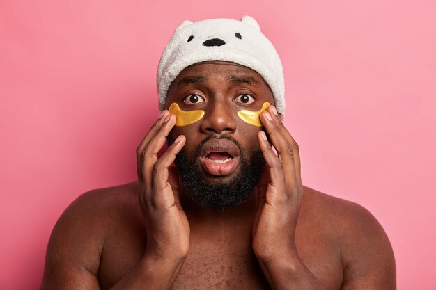 Afro American man with clay mask, expresses positive emotions isolated