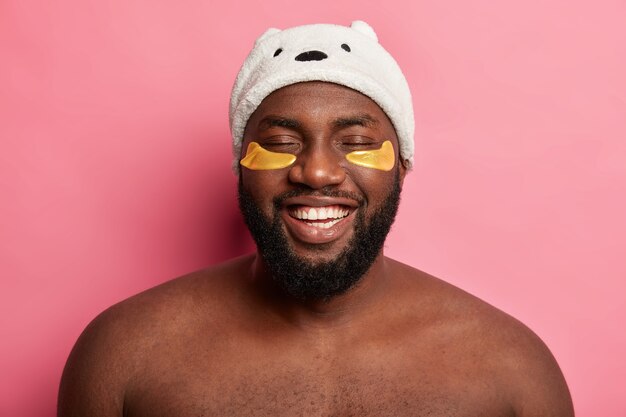 Afro American man with clay mask, expresses positive emotions isolated