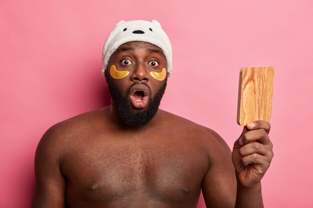 Afro American man with clay mask, expresses positive emotions isolated