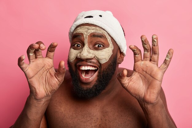 Afro American man with clay mask, expresses positive emotions isolated